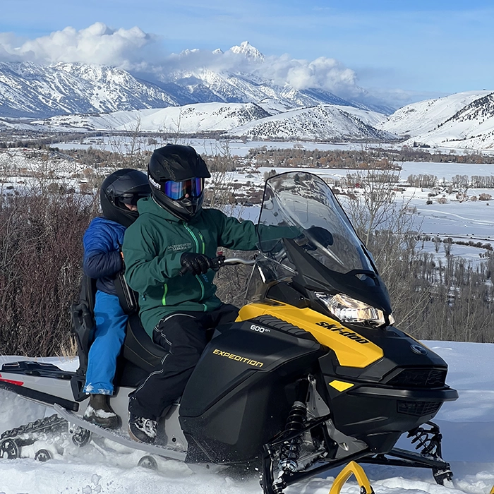 Jackson Hole Snowmobile Guide and Child on Snowmobile with the Tetons in the Background